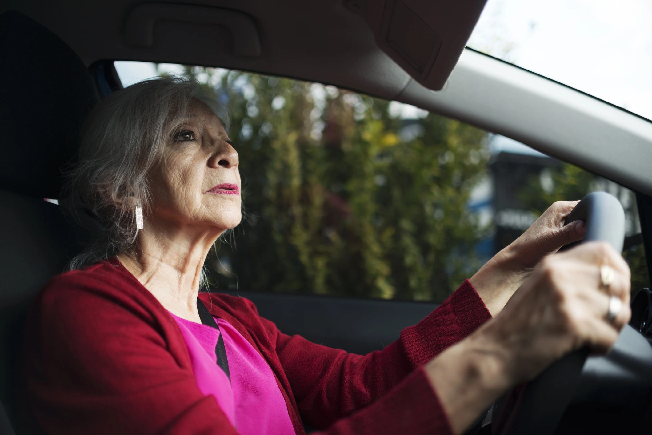 senior woman wearing pink driving a car